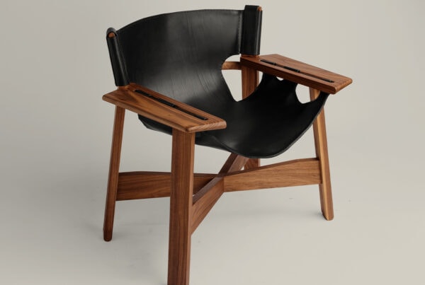 Butaca More de cuero negro con estructura y reposabrazos de nogal macizo, asiento tipo sling.