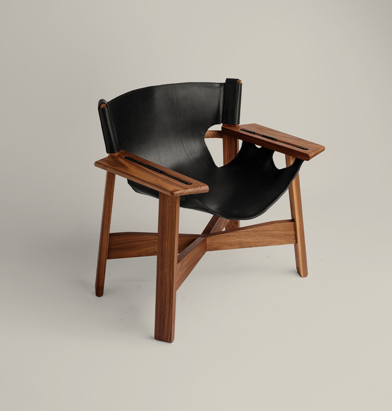 Butaca More de cuero negro con estructura y reposabrazos de nogal macizo, asiento tipo sling.